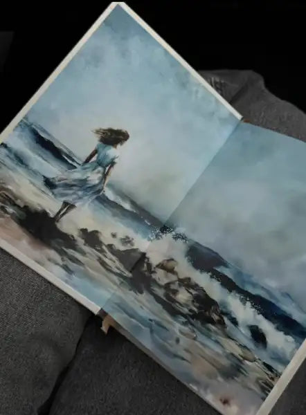 Open art book featuring a woman painting on a stormy beach for Evening with Kiose Marina 2025 Open art book featuring a woman painting on a stormy beach for Evening with Kiose Marina 2025