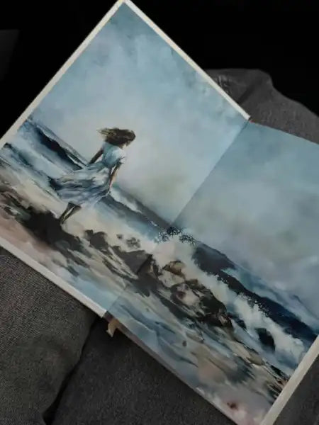 Open book featuring Marina Kiose painting of a woman on a stormy beach in English books Open book featuring Marina Kiose painting of a woman on a stormy beach in English books