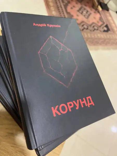 Stack of dark-colored books with a red crystal design from Korund by Andrii Krupkin